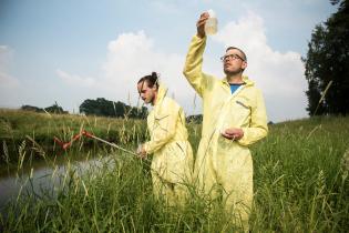 Zwei Aktivisten in gelben Anzügen nehmen Wasserproben aus einem Fluss