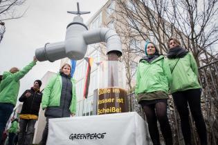 Aktivist:innen neben Installation: aus überdimensioniertem Wasserhahn fließt symbolisch mit Gülle verdrecktes Wasser 