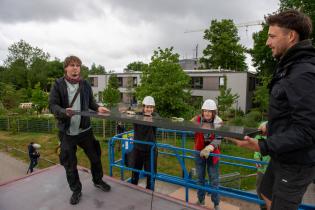 Vier Personen tragen ein Solarpanel von einer Hebebühne auf das Dach