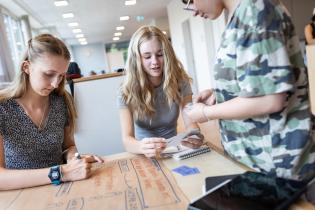 Drei Schüler:innen sitzen an einem Tisch und schreiben ein Plakat