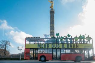 Aktivist:innen auf einem roten, nach oben geöffneten Doppeldeckerbus, am Bus steht: „Mehr Bus & Bahn“