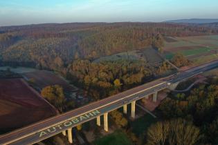 Auf einem noch nicht freigegebenen Bauabschnitt steht mit Kreidefarbe ein 90 Meter lange Schriftzug "AUTOBAHN" mit durchgestrichenem ersten Wortteil “Auto”.