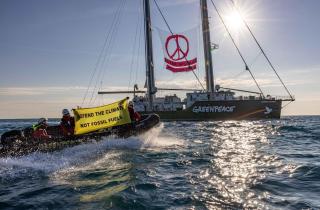 Aktivist:innen von Greenpeace Italien an Bord des Schiffes Rainbow Warrior prangern Militärmissionen zum Schutz fossiler Brennstoffe an. Auf Transparenten: "Verteidigt das Klima, nicht die fossilen Brennstoffe".