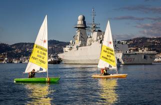 Aktivist:innen von Greenpeace Italien an Bord des Schiffes Rainbow Warrior prangern Militärmissionen zum Schutz fossiler Brennstoffe an. Auf Transparenten: "Verteidigt das Klima, nicht die fossilen Brennstoffe".