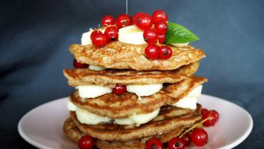 Ein Turm aus Pfannkuchen dekoriert mit Bananen und Johannisbeeren.