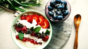 Appetitlich angerichtet zwei Schalen mit Erdbeeren, Blaubeeren, Himbeeren und Johannisbeeren. Darüber gestreut Kokosflocken und Amaranth, garniert mit Pfefferminzblättern.