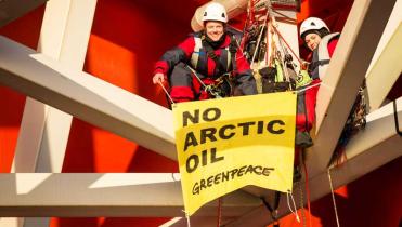 Zwei Greenpeace-Aktivistinnen im Gestänge der Plattform Transocean Spitsbergen. Sie sind angeseilt, tragen Sicherheitshelme und halten ein Banner mit der Aufschrift "No arctic oil"