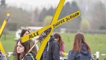 Frau auf Demo mit gelbem Kreuz, auf dem "Alle Dörfer bleiben" steht