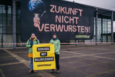 Aktive hängen Banner an Fassade "Zukunft nicht verwursten" steht neben einer Erdkugel, die durch den Fleischwolf gedreht wird.