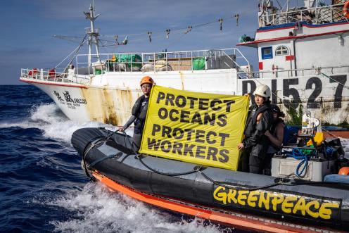 Greenpeace-Forschungsreise im Nordpazifik: Aktivist:innen und Forscher:inen protestieren für menschenwürdige Arbeitsbedingungen vor einem taiwanesischen Langleinenfischer (03/2023). Sie halten ein Banner mit der Aufschrift: "Protect Oceans Protect Workers"