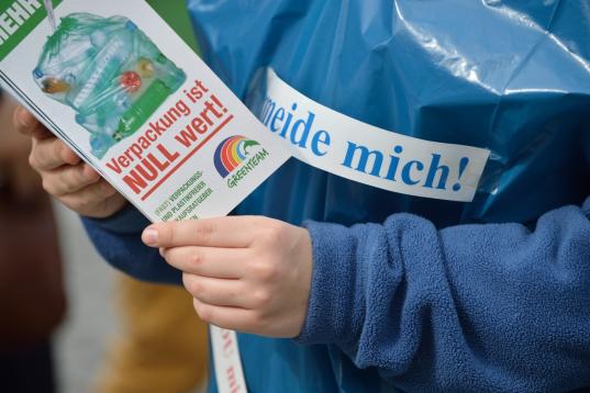 Nahaufnahme von Flugblättern. Kinder mehrerer Greenteams informieren die Öffentlichkeit über die Verschmutzung der Ozeane durch Plastikmüll. Sie stehen neben einem großen Haufen Plastik.