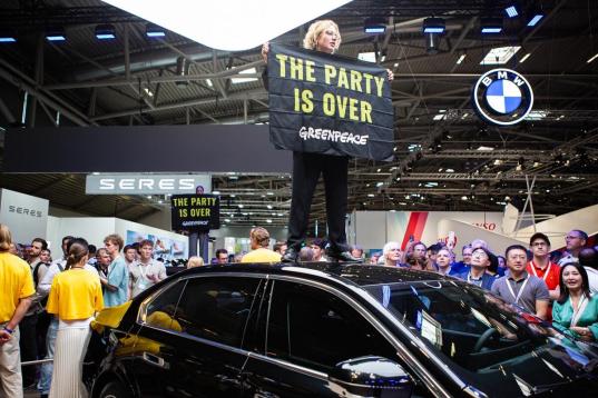 IAA: Aktivist:in steht auf einem Autodach und hält ein Banner "The party is over"