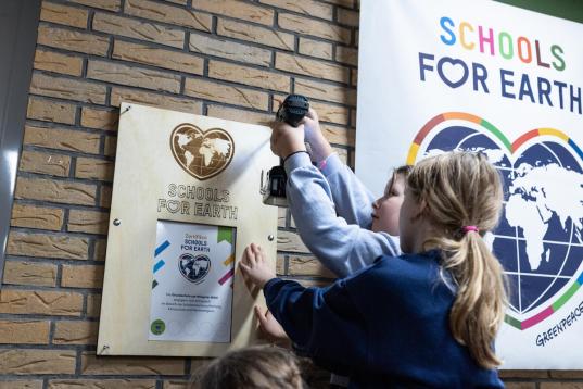 Zwei Mädchen bringen eine Holzplakette an die Wand. Daneben hängt ein Plakat von Schools for Earth