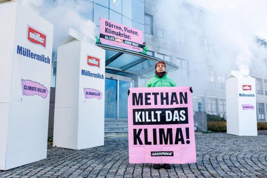 Protest vor Molkerei Müller in Aretsried: aus übergroßen Milchtüten quillt weißer Rauch, auf dem Banner steht "Methan killt das Klima".