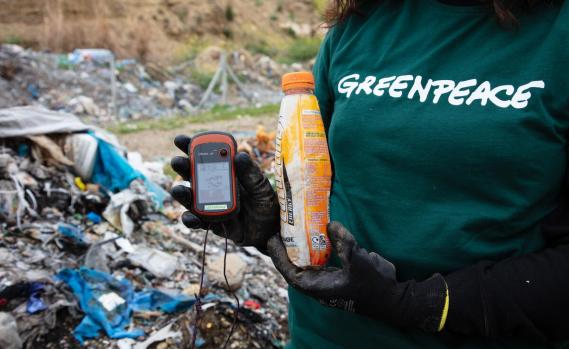 Greenpeace-Aktivistin hält ein GPS-Gerät und eine Plastikflasche auf einer Mülldeponie in der Türkei.