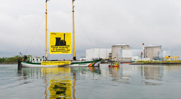 Das Greenpeace-Schiff Beluga II fährt vor dem französischen Atomkraftwerk Fessenheim vorbei. Zwischen den beiden Masten und den Aktivist:innen im Schlauchboot weht ein Banner mit der Botschaft "Europa nicht länger auf's Spiel setzen!". Ein zweiter Banner zeigt die Botschaft in französischer Sprache: "Schaltet alternde Kraftwerke ab!"