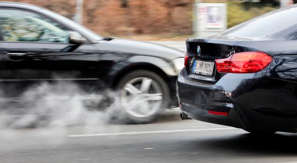 Zwei Autos auf der Straße, aus dem Auspuff quellen Abgase