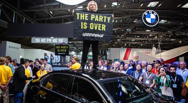 Aktivist:in hält auf der IAA ein Banner auf einem Autodach: The party is over