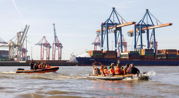 Schüler sitzen in Schlauchbooten auf der Elbe vor den Hafenkränen