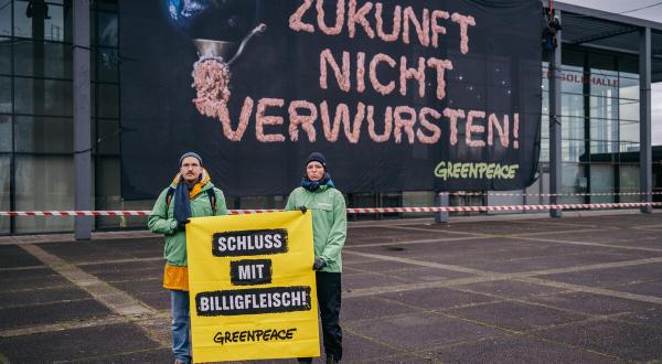 Aktive hängen Banner an Fassade "Zukunft nicht verwursten" steht neben einer Erdkugel, die durch den Fleischwolf gedreht wird.