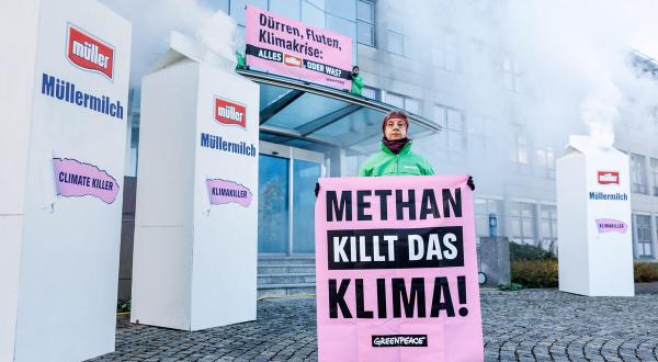 Protest vor Molkerei Müller in Aretsried: aus übergroßen Milchtüten quillt weißer Rauch, auf dem Banner steht "Methan killt das Klima".