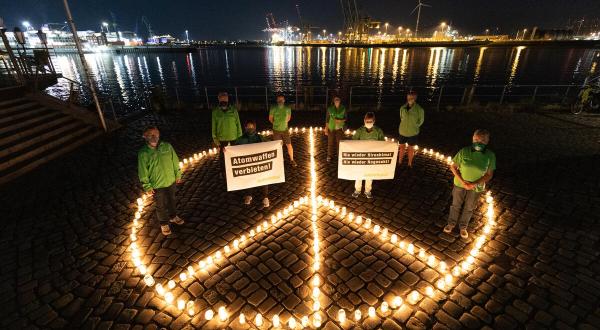 Peacezeichen aus Kerzen im Dunkeln, darin gegen Atomwaffen protestierende Greenpeace-Aktive