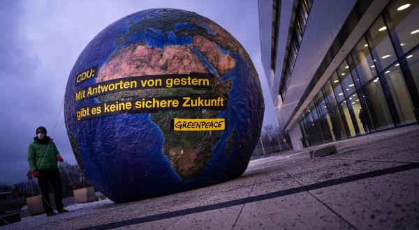 Protest  auf CDU-Parteitag. Aktivist:innen stehenneben einem fünf Meter hohen Ballon in Form einer Weltkugel mit Aufschrift: "CDU: Mit Antworten von gestern gibt es keine sichere Zukunft."