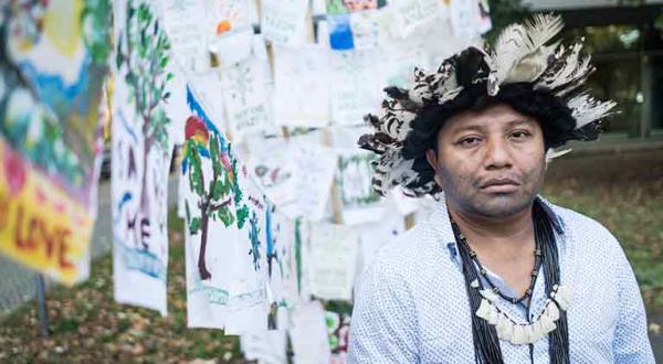 Indigenensprecher Adriano Karipuna vor der brasilianischen Botschaft. Im Hintergrund kleine Flaggen, die Menschen aus ganz Deutschland in den vergangenen Monaten gestaltet und an die brasilianische Regierung adressiert haben.