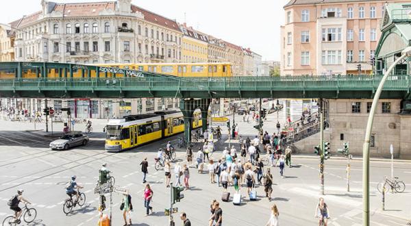 Verkehr in Berlin: S-Bahn, Straßenbahn, Fußgänger und Fahrradfahrende auf einer Kreuzung.