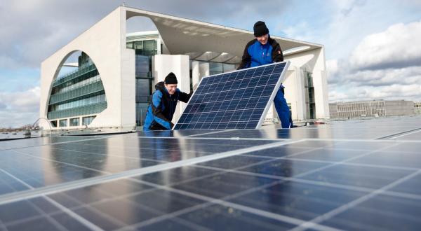 Arbeiter installieren Photovoltaikanlage auf Dach vor Reichstag in Berlin