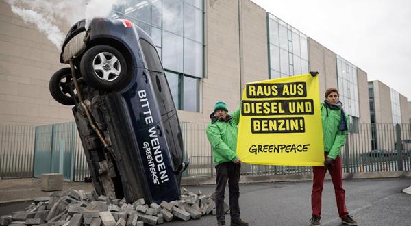 Mit einem schräg im Boden steckenden Auto demonstrieren Greenpeace-Aktivisten vor dem Bundeskanzleramt für Klimaschutz im Verkehr. Der Wagen mit qualmendem Auspuff trägt die Aufschrift „Bitte wenden!“