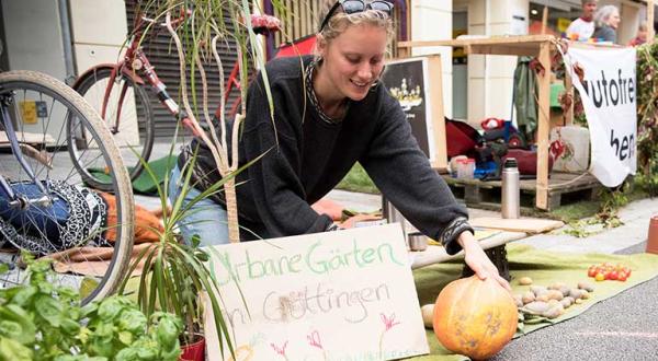 Park(ing) Day: eine Frau breitet einen Kürbis, Kartoffeln und Tomaten auf einer Decke aus, wo sonst Autos parken.