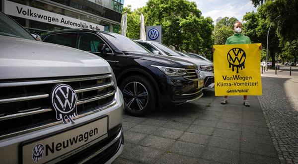 Aktivist steht vor einem VW-Händler und hält ein Banner mit der Aufschrift "Von Wegen Klima-Vorreiter!"