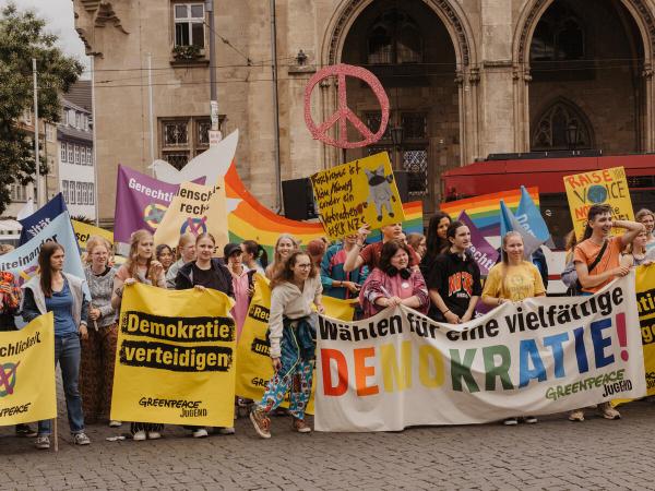 Junge Menschen demonstrieren mit Plakaten in der Hand wie "Demokratie verteidigen"