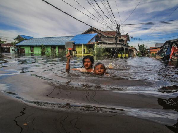 Kinder schwimmen/waten durch die Fluten: Überschwemmungen in Palangka Raya, Zentral-Kalimantan