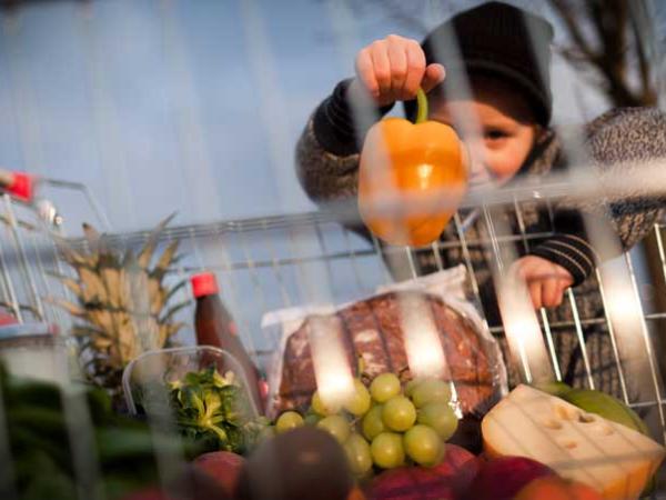 Kind schaut durch einen Einkaufskorb, in dem Obst liegt.